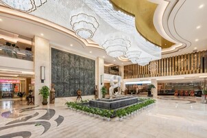 Un lobby espacioso con una fuente central, techos altos con diseños intrincados y un estilo arquitectónico moderno.