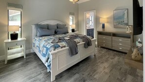 Une chambre à coucher comprenant un lit, des tables de chevet, une commode, un ventilateur de plafond et un tableau accroché au mur.