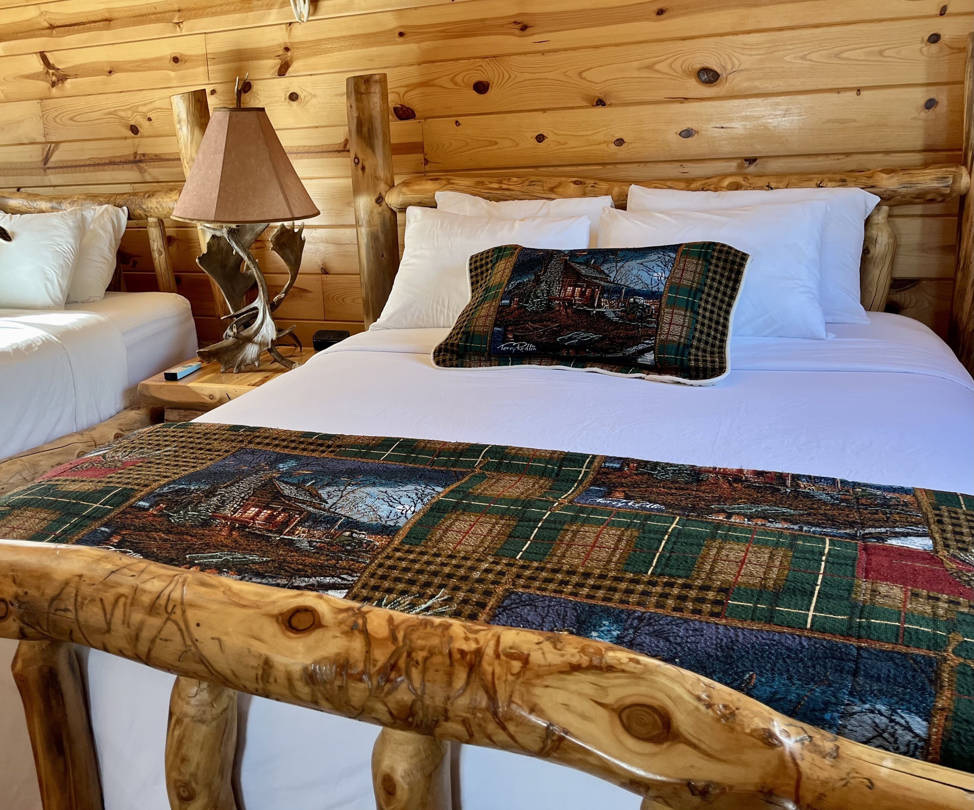 A wooden cabin-style bedroom with a large bed, white bedding, and a colorful quilt.
