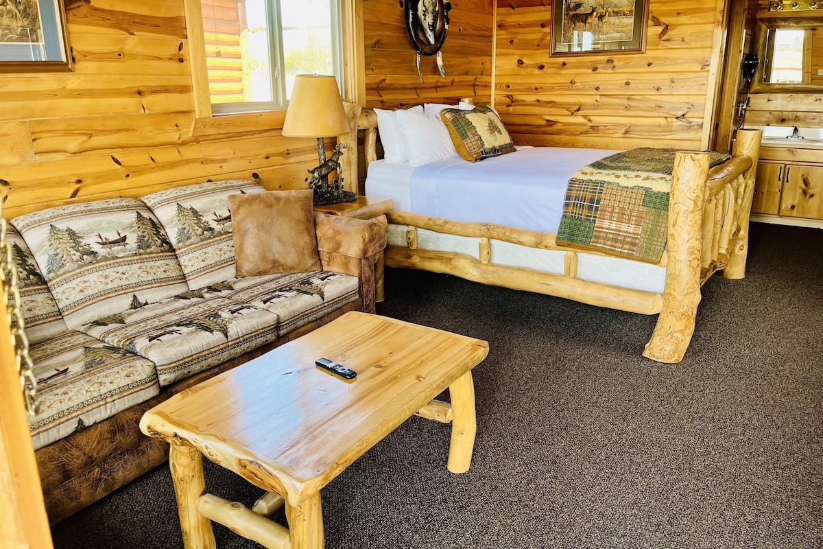 A wooden cabin interior with a bed, sofa, and a small table.