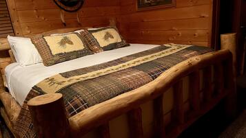 A wooden bed with a quilt and pillows, a wooden headboard, and a framed picture on the wall.