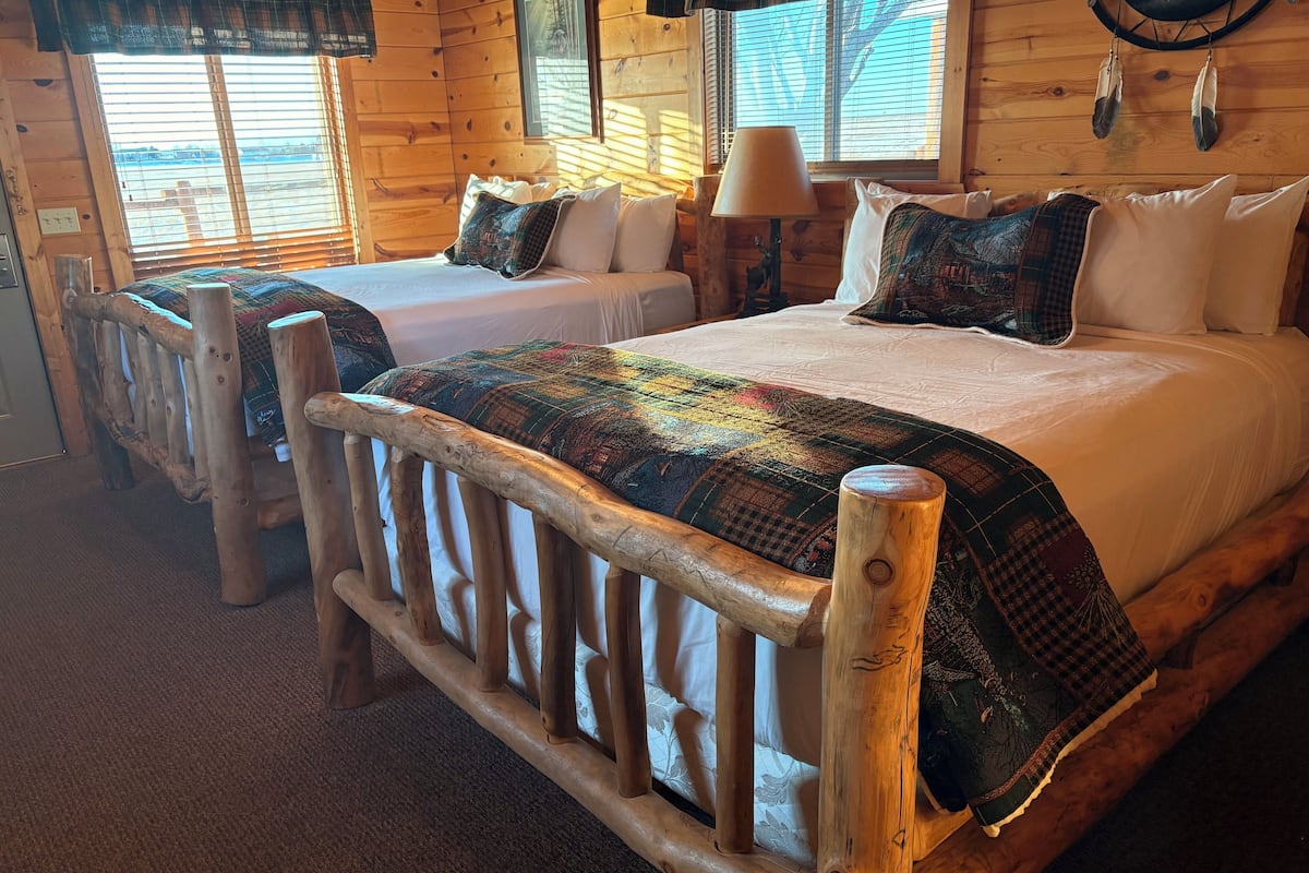 A cabin-style room with two wooden beds, each with a unique patterned blanket.