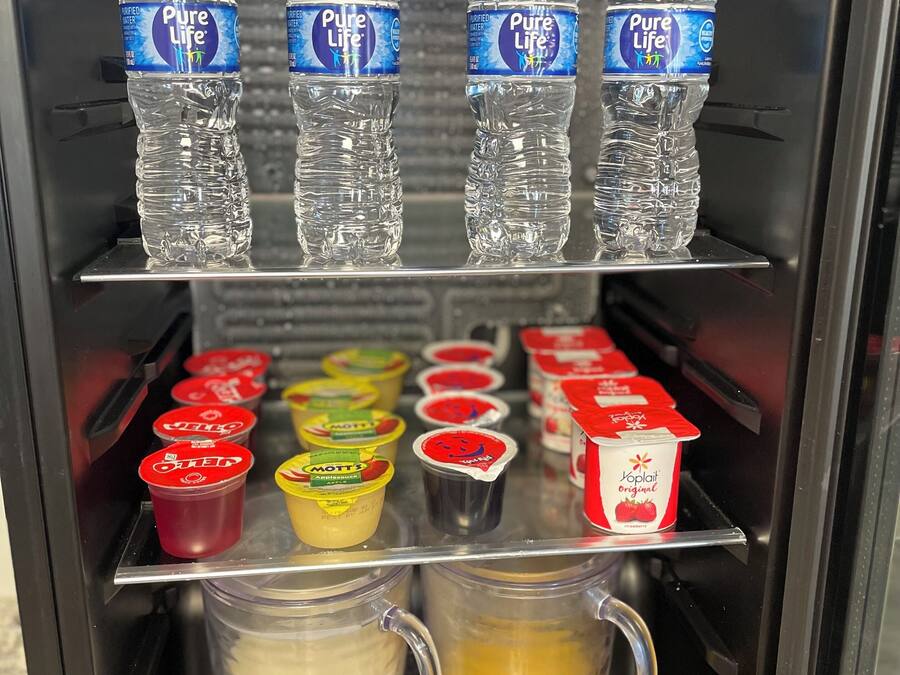 A beverage dispenser with bottled water, yogurt cups, and milk and juice containers.