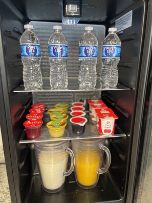 A beverage dispenser with bottled water, yogurt cups, and milk and juice containers.