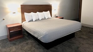 Una cama con cuidada presentación, un cabecero de madera, dos mesitas de noche y lámparas de pared.