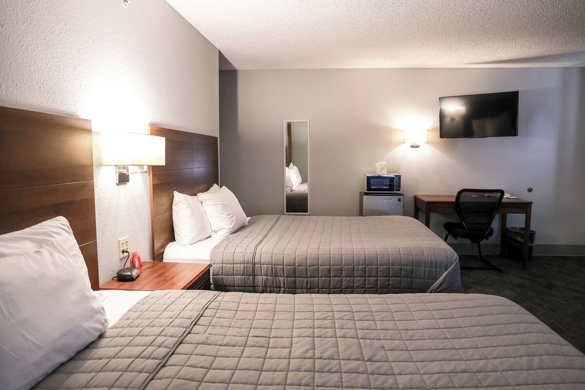 A hotel room with two beds, a desk, a chair, a TV, and a mirror.