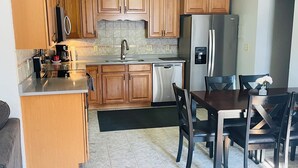 Una cocina con armarios de madera, un refrigerador de acero inoxidable, un lavavajillas y una mesa de comedor con sillas.