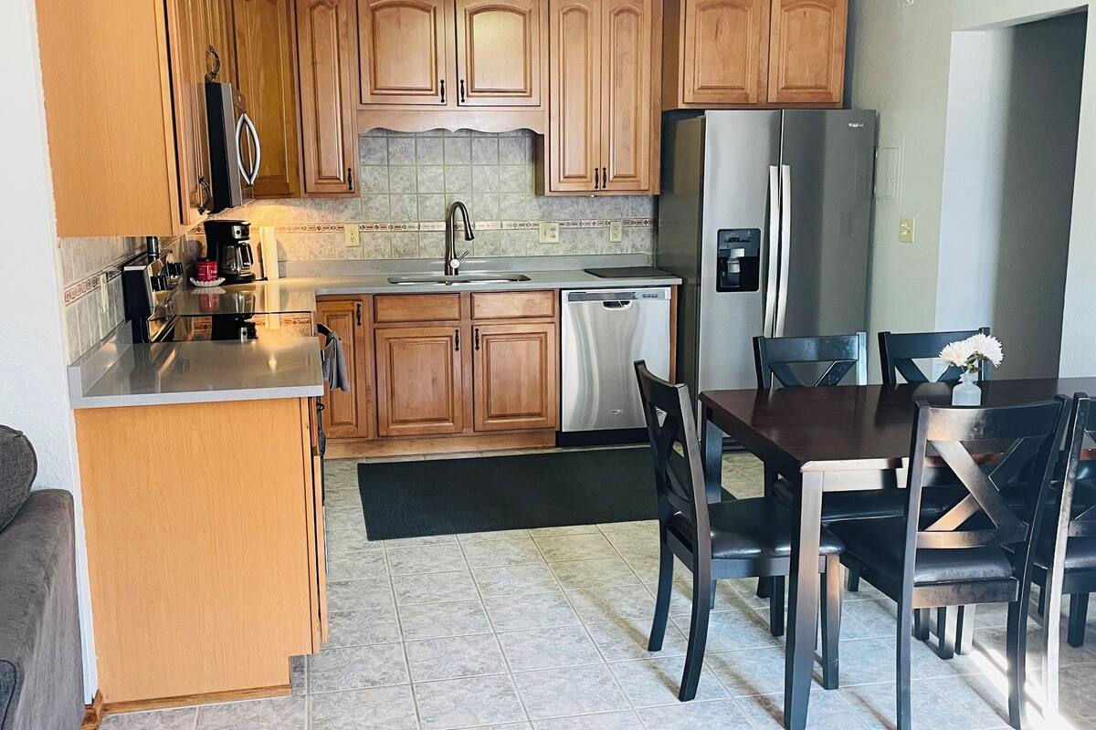 A kitchen with wooden cabinets, a stainless steel refrigerator, a dishwasher, and a dining table with chairs.