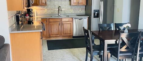 A kitchen with wooden cabinets, a stainless steel refrigerator, a dishwasher, and a dining table with chairs.