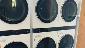 Una hilera de lavadoras de carga frontal blancas con puertas negras, dispuestas en una sala de exposición.