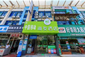 A building with a prominent green sign for a hotel, multiple air conditioning units, and various storefronts including a pharmacy. - Hi Inn (Shanghai Zhangjiang Park) (Shanghai)