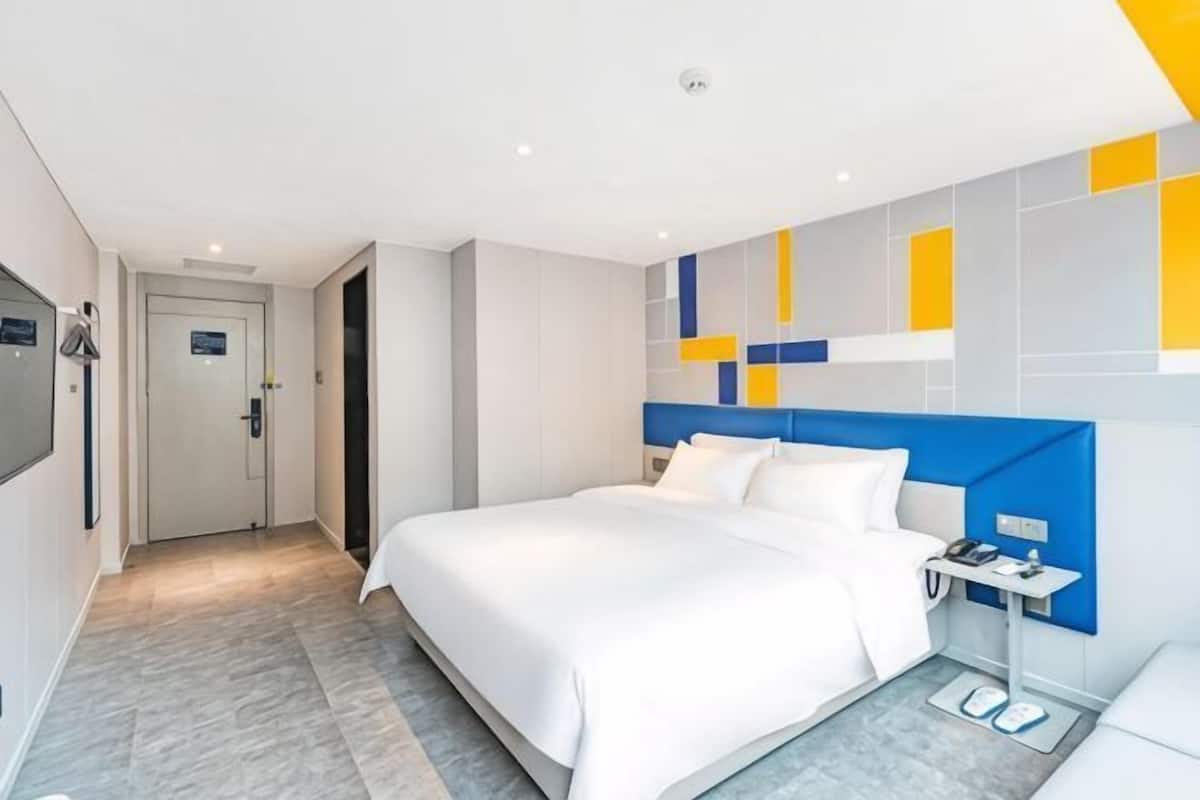 A hotel room with a bed, bedside table, and a wall-mounted TV.