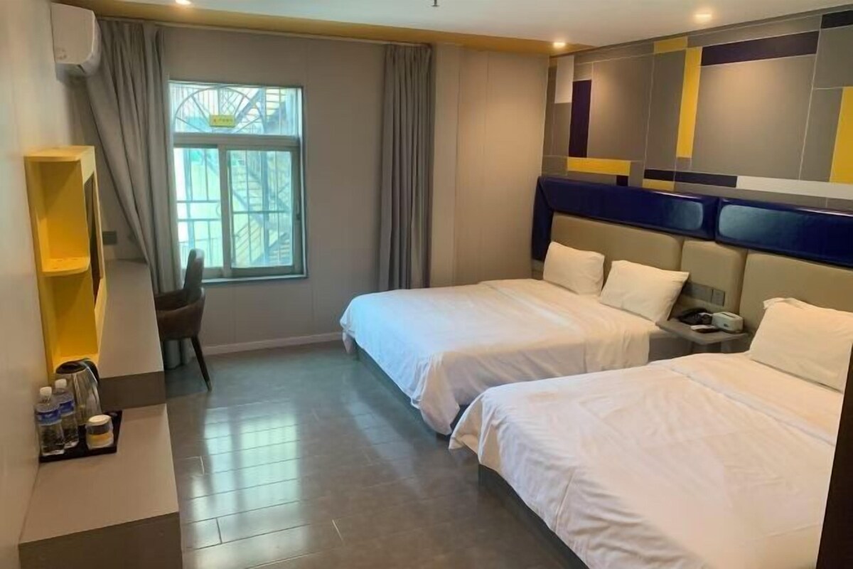 Ein Hotelzimmer mit zwei Betten, einem Schreibtisch, einem Stuhl, einem Fenster mit Vorhängen und einer Wand mit geometrischem Muster.