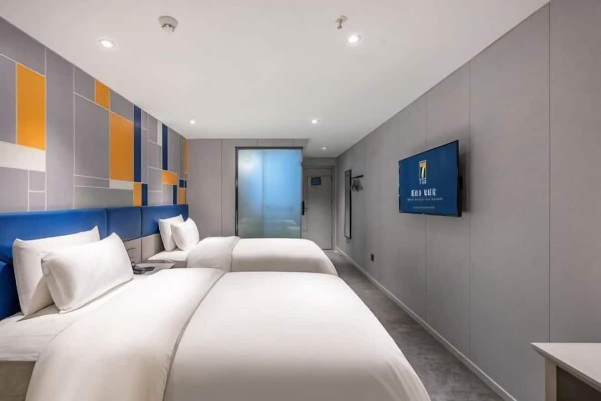 A hotel room with two beds, a television, and a view of the hallway.
