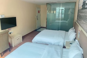 Ein Hotelzimmer mit zwei Betten, einem Fernseher, einem kleinen Schreibtisch und einer Duschkabine.