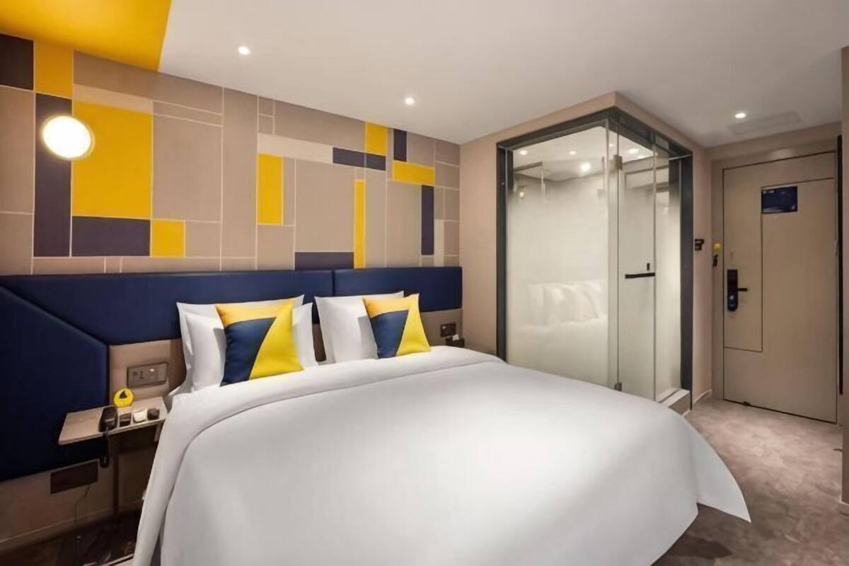 A hotel room with a bed, a nightstand, a glass door, and a door with a sign.