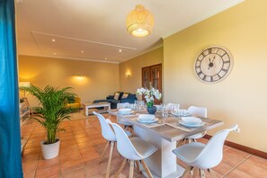Un coin repas avec une table dressée pour quatre personnes, une horloge au mur et une plante dans un coin.