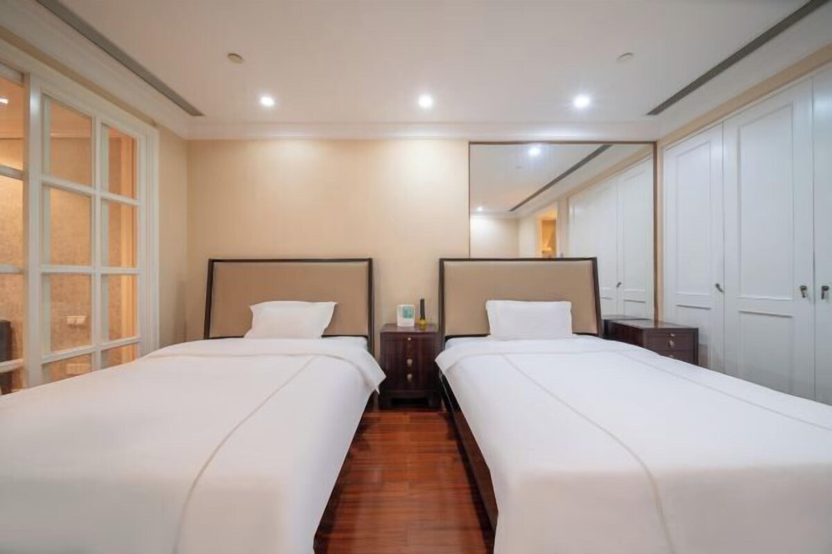 A hotel room with two beds, a wooden floor, a nightstand, a mirror, and a wardrobe.