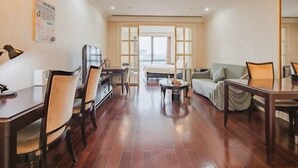 Una habitación de hotel con comedor, sofá, televisor y un amplio ventanal.
