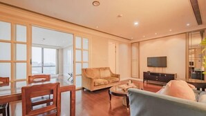 Amplia sala de estar con sofá, una mesita de centro y televisor. Hay una mesa de comedor con sillas y un ventanal con vistas.