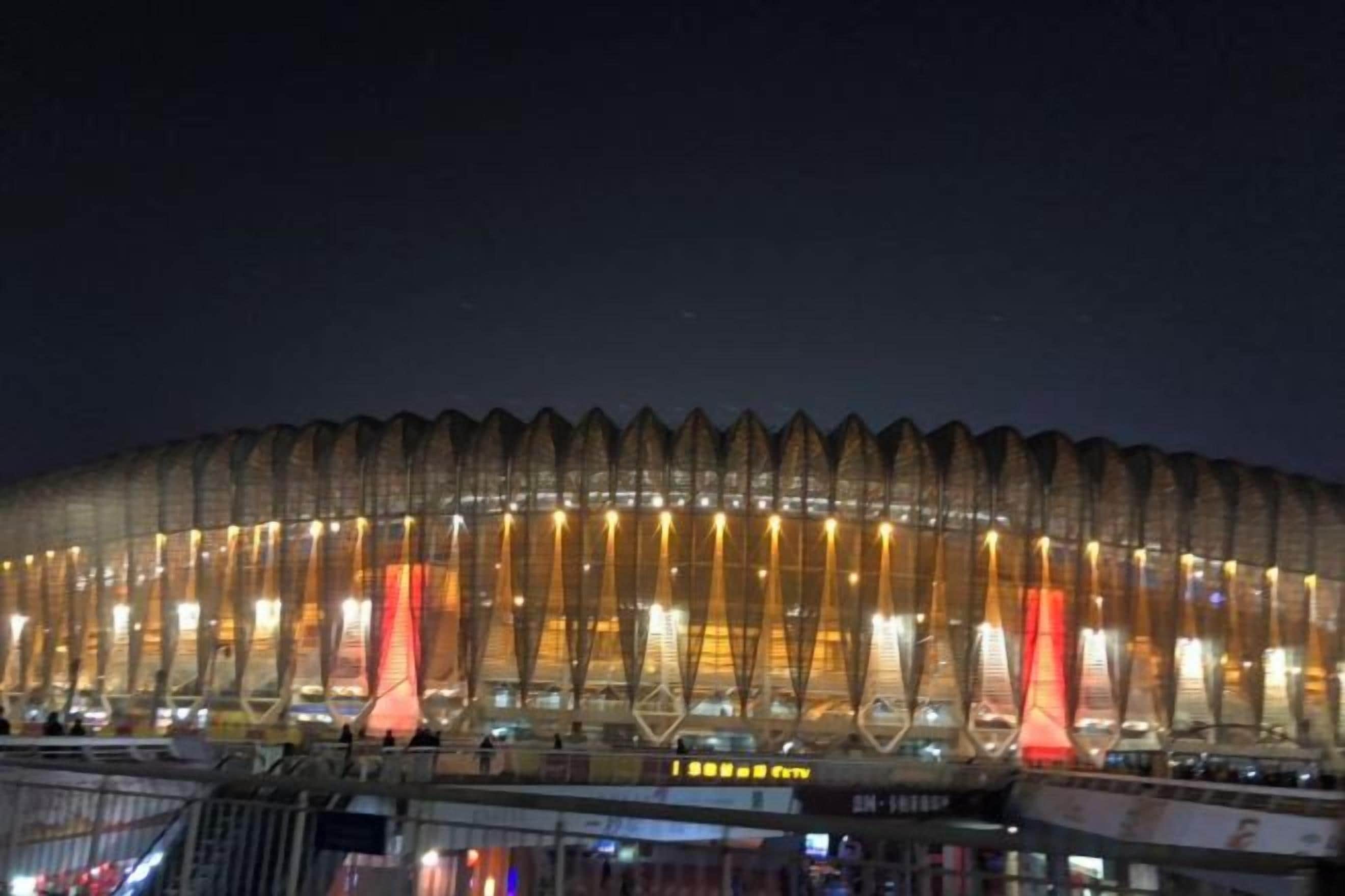 A large, illuminated stadium with a distinctive roof structure and multiple light sources.