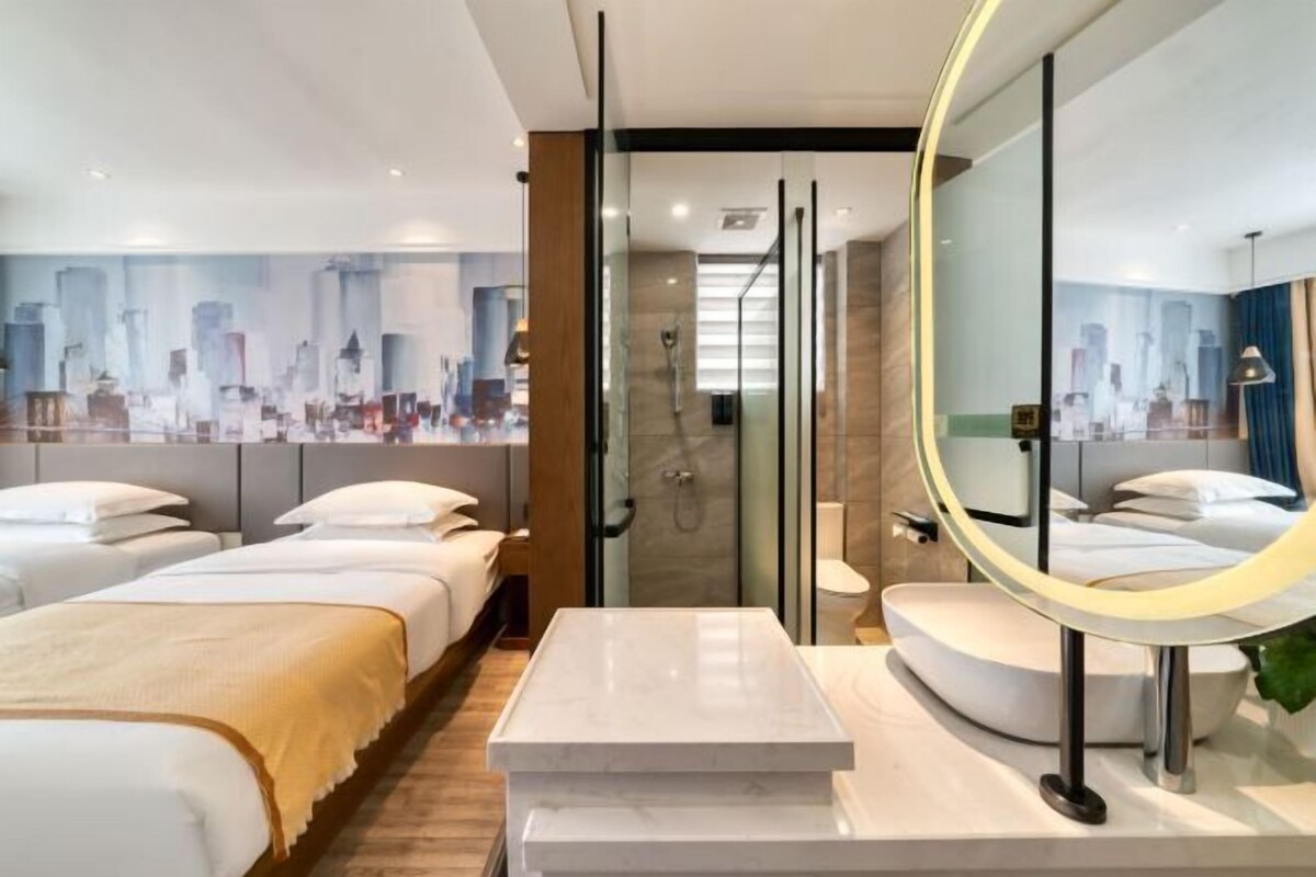 Una habitación de hotel moderna con dos camas, un baño con ducha de vidrio y un espejo grande.