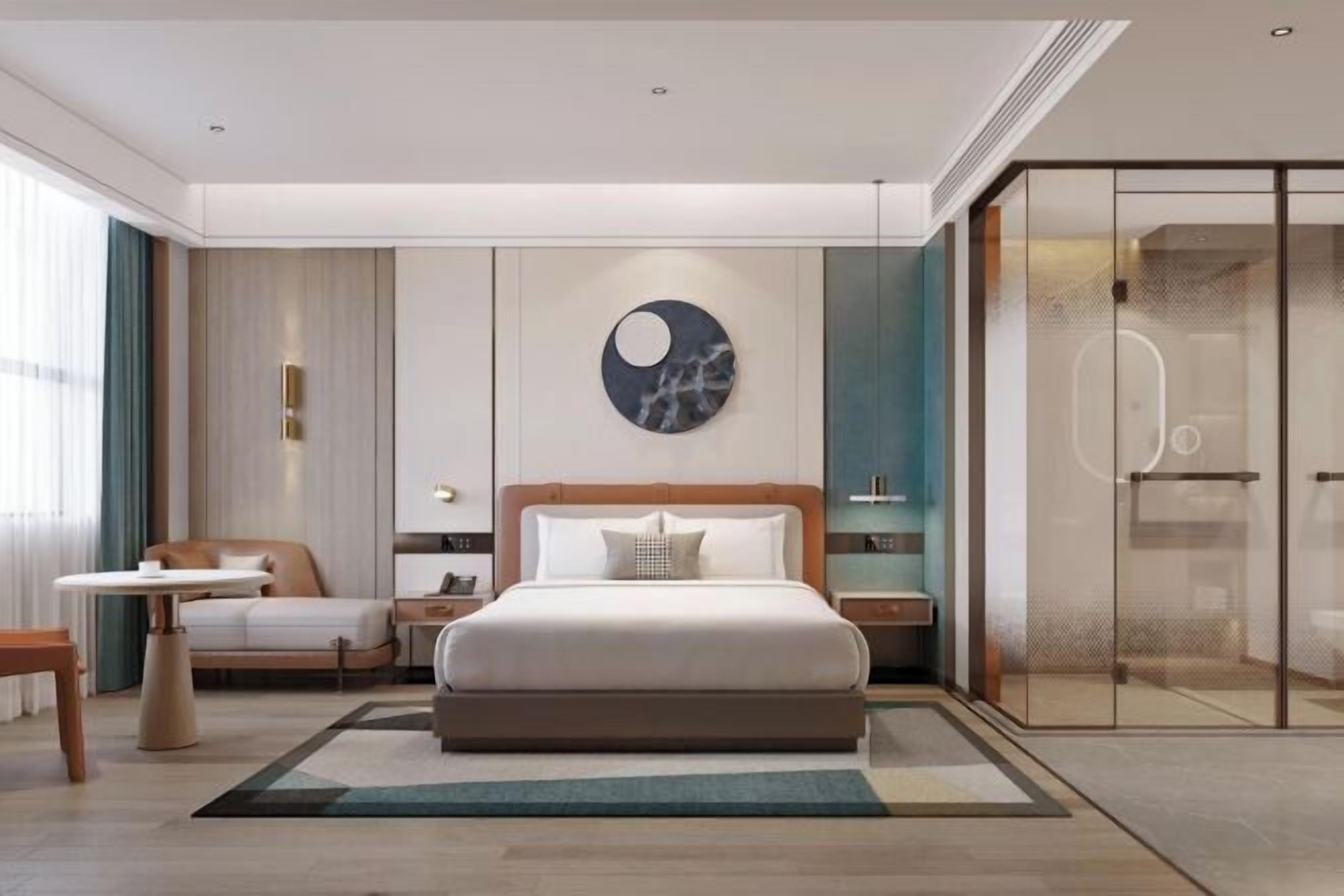 Habitació d'hotel moderna amb un llit gran, una obra d'art rodona a la paret, un espai de banyera amb dutxa i una zona de seients amb una taula.
