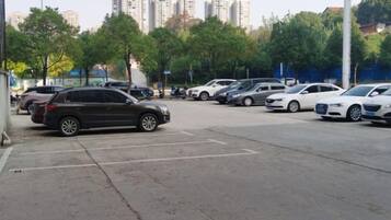Un estacionamiento con varios autos, árboles y edificios al fondo.