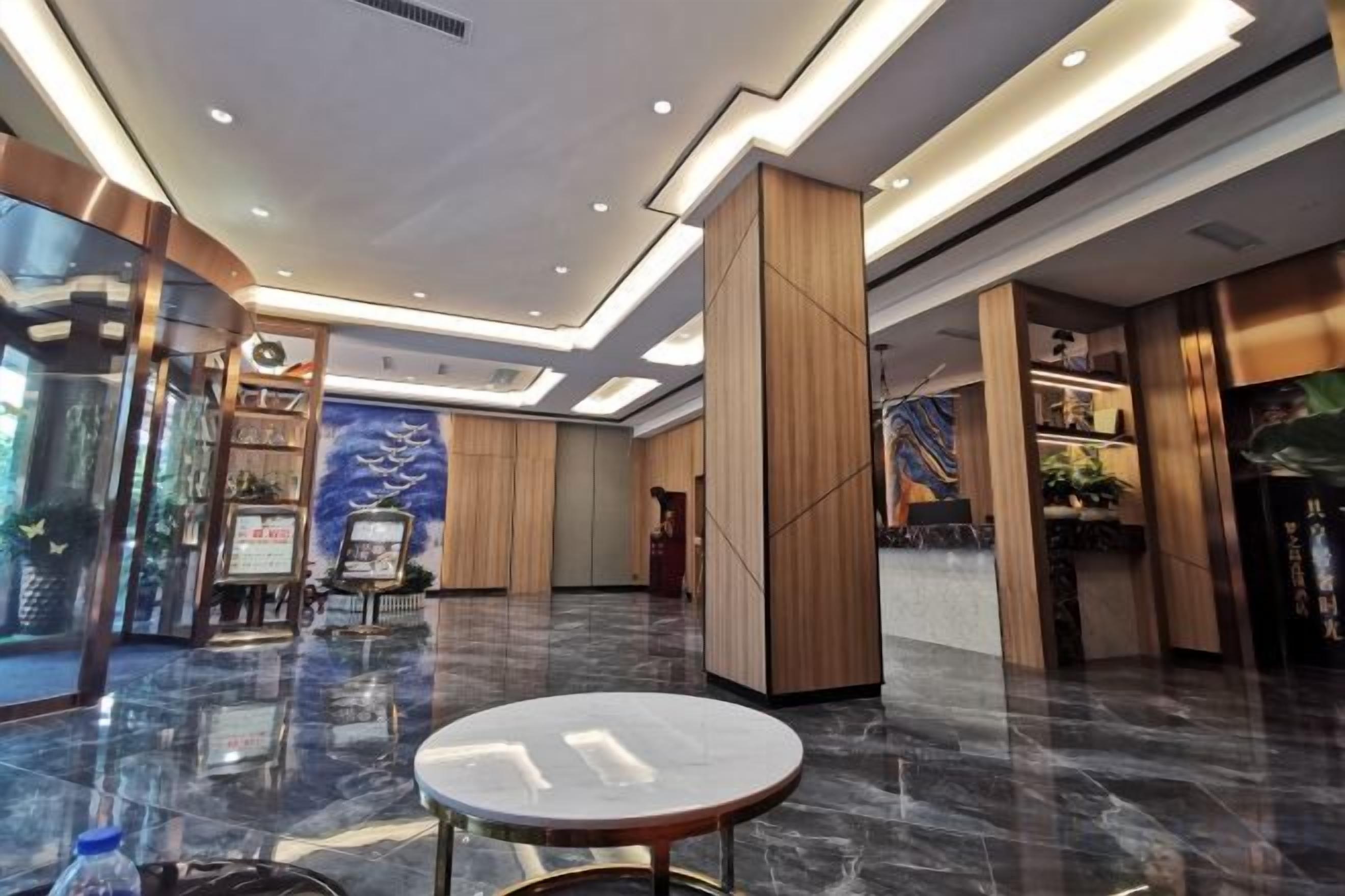 Een hotellobby met een marmeren vloer, een receptiebalie en een grote houten zuil.