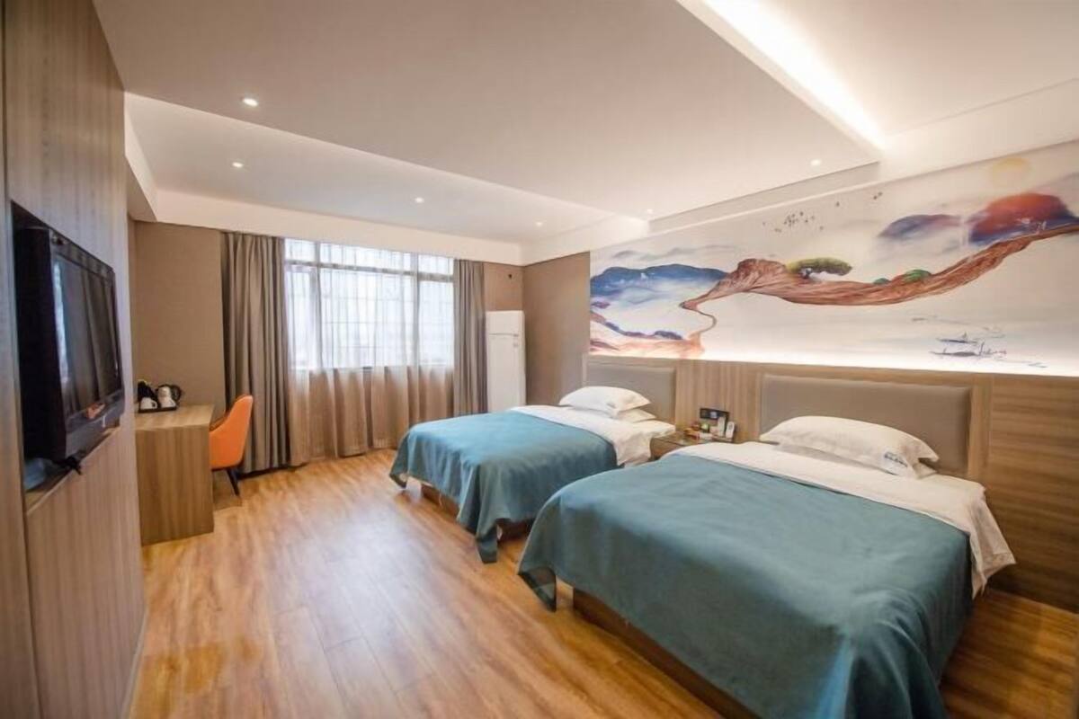 Une chambre d’hôtel avec deux lits, un bureau, une télévision et une fresque murale.
