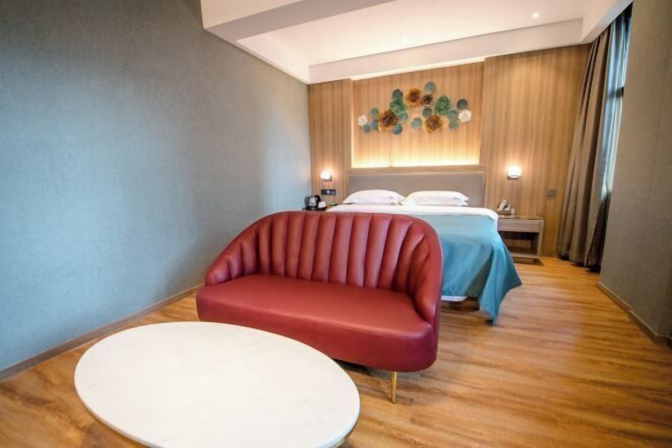 Una habitación de hotel moderna con un sofá rojo, una mesa redonda, una cama con colcha azul y un elemento decorativo en la pared.