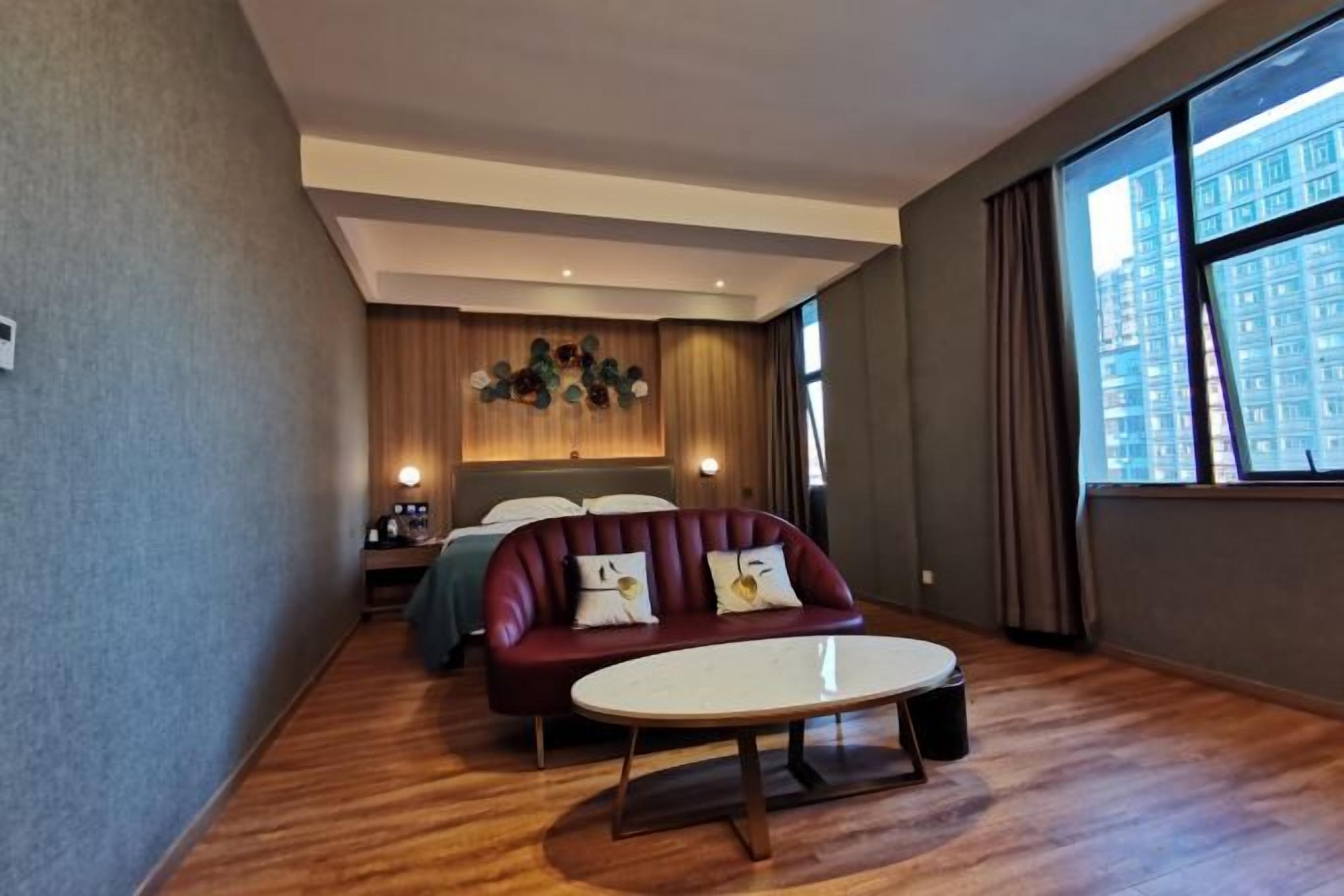 A hotel room with a sofa, a small table, a bed, and a large window.