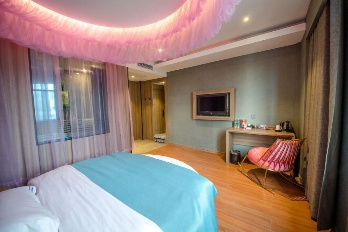 A hotel room with a bed, a desk, a chair, and a television.