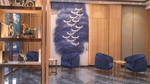 A lobby with a wooden reception desk, a wall mural, and blue seating. - Meng Zhi Dao Hotel (Loudi)
