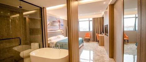 A modern hotel room with a large bathtub, a separate shower area, a bed, a seating area with a chair, and a large window offering a city view.
