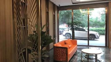 A lobby with a modern design, featuring a sofa and a small table, and large windows offering a view of the outside.