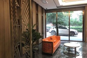 A lobby with a modern design, featuring a large window, a seating area with an orange sofa, and a decorative wall panel. - Meng Zhi Dao Hotel (Loudi)