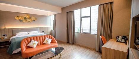 A modern hotel room with a bed, orange sofa, and a small wooden desk.