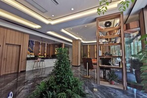 A hotel lobby with a reception desk, seating area, and a large bookshelf.