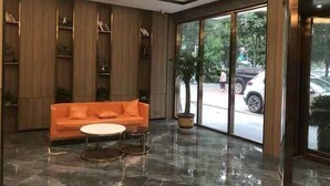 A modern lobby with a wooden panel wall, a glass door leading outside, a round table, and an orange sofa. - Meng Zhi Dao Hotel (Loudi)