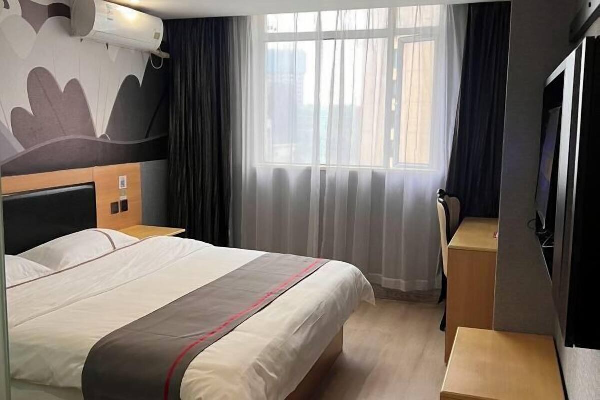 Une chambre d’hôtel avec un lit, un bureau, une télévision et une fenêtre avec des rideaux.