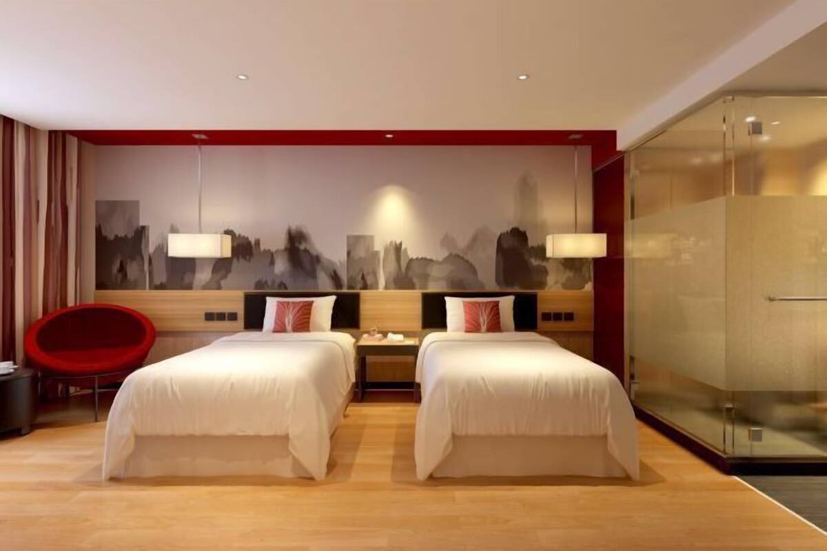 Une chambre d’hôtel avec deux lits, une chaise rouge, une table de chevet et une fresque représentant un paysage urbain sur le mur.
