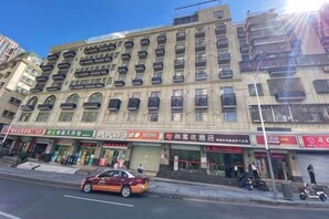 Un immeuble à plusieurs étages, avec des commerces au rez-de-chaussée, une voiture garée et un trottoir pour les piétons.