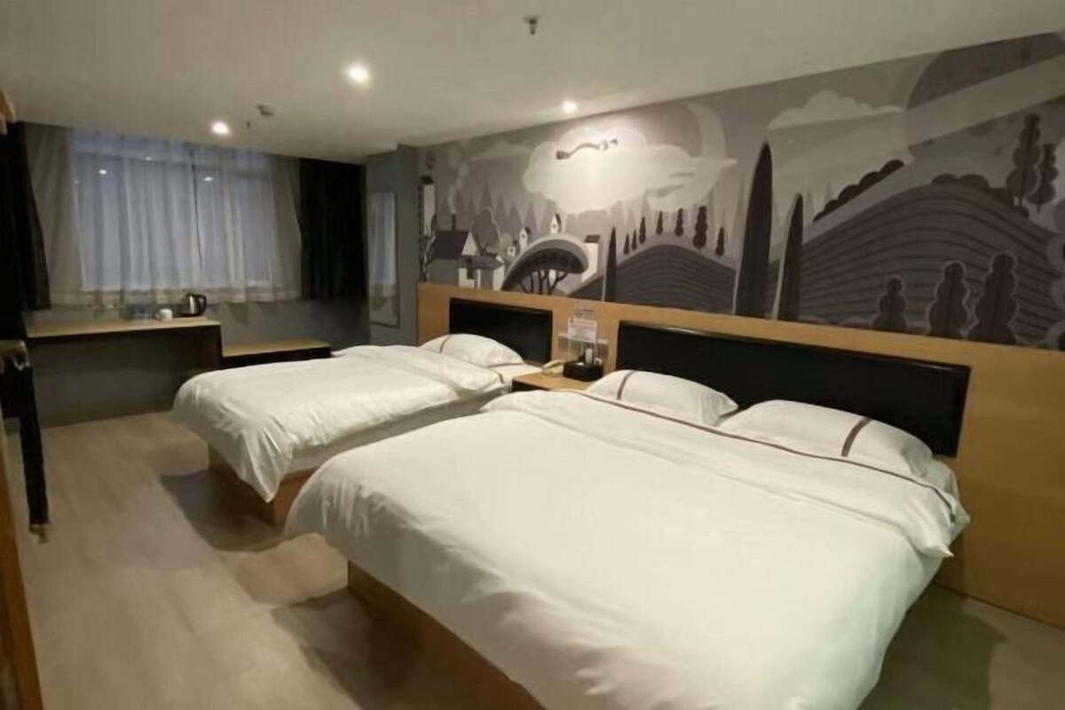 Une chambre d’hôtel avec deux lits, une grande fenêtre avec des rideaux, une fresque murale et une table de chevet avec une lampe.