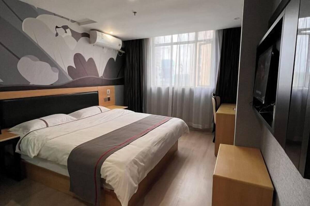 Une chambre d’hôtel avec un lit, une télévision, une fenêtre avec des rideaux et un mur orné d’un grand motif abstrait.