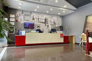 A reception desk with a digital screen, a receptionist, and a cityscape mural on the wall.