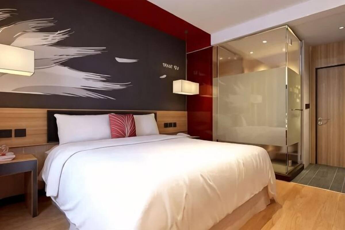 Une chambre d’hôtel moderne dotée d’un grand lit, d’une douche en verre et d’une œuvre d’art murale originale.