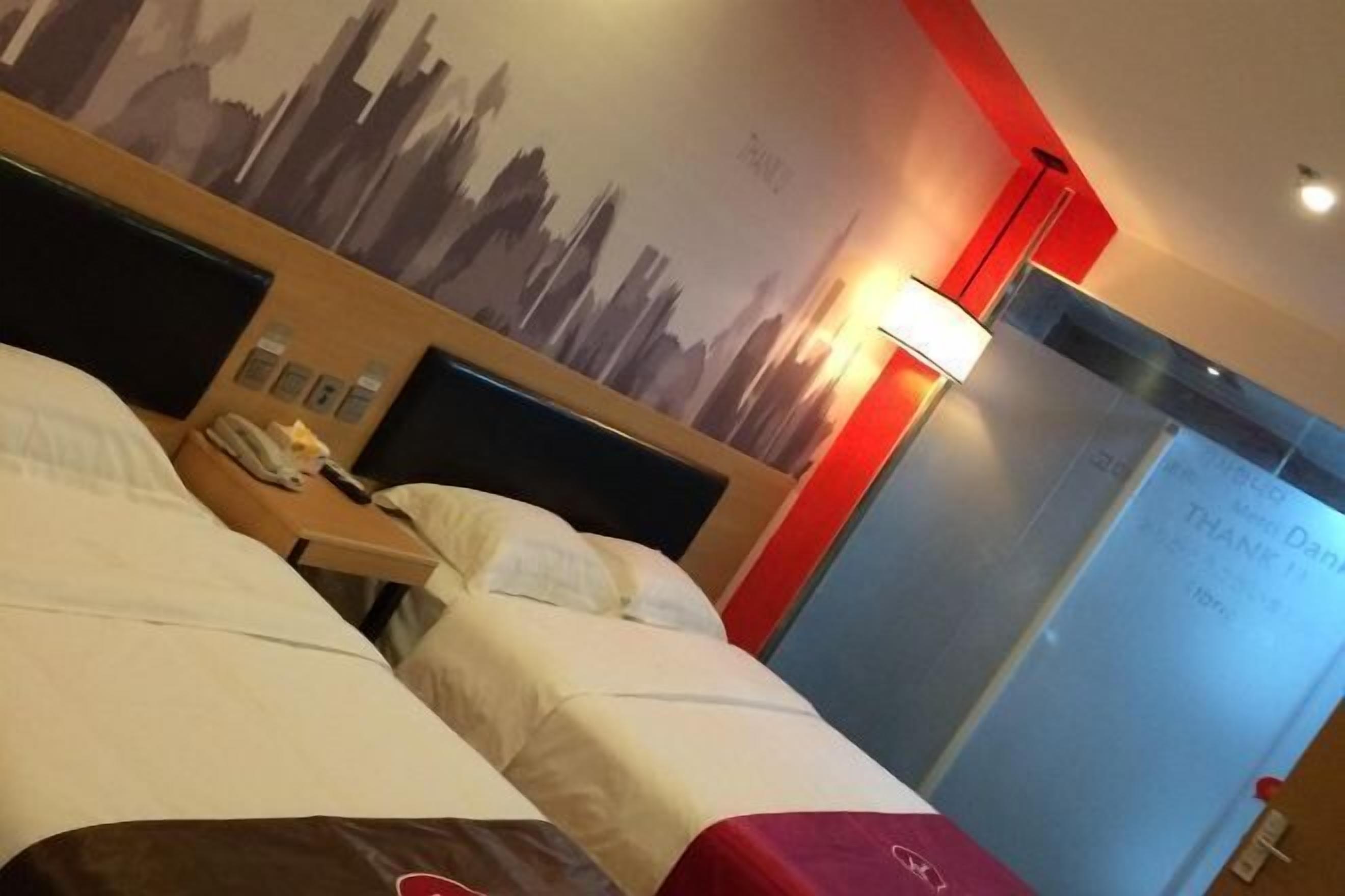 A hotel room with two beds, a nightstand, a lamp, and a wall with a cityscape mural.