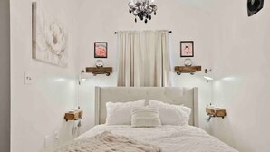 A bedroom with a large bed, a chandelier, and artwork on the walls. - Fox Cottage *Pet Friendly* (Catonsville)