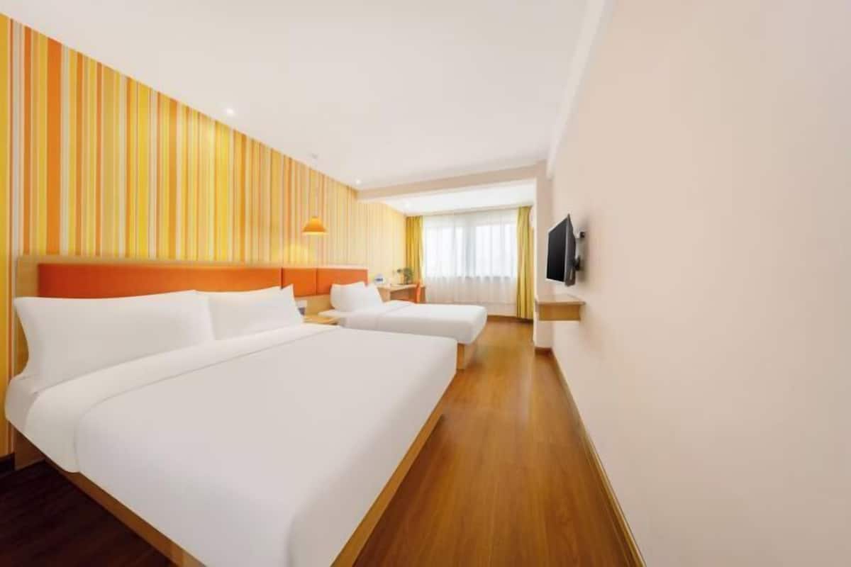 A hotel room with two beds, a wooden floor, a striped wall, and a TV on the wall.